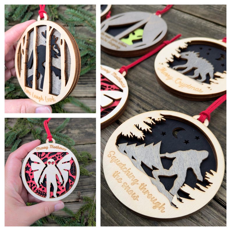 May include: Wooden Christmas ornaments with various designs. One features a deer in a forest, another a cryptid, and a third a mothman. Each ornament has a red ribbon for hanging and includes text like "Love Laugh Lurk" and "Merry Cryptmas".