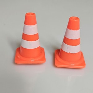 May include: Two orange traffic cones with white reflective stripes. The cones have a square base and a cylindrical top. The cones are used for traffic control and safety.
