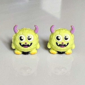 以下が含まれることがあります： モンスター型のピアス。各ピアスは黄色の体、紫の角、白黒の目があります。ピアスは笑顔の口とオレンジ色の足を持っています。これらは楽しいアクセサリーです。