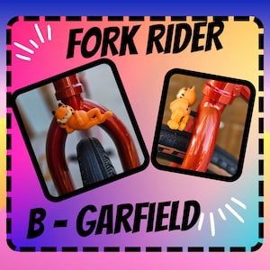 May include: A red bicycle fork with a black tire and a Garfield character figurine attached to the fork. The text "FORK RIDER" is at the top of the image and "B - GARFIELD" is at the bottom of the image.