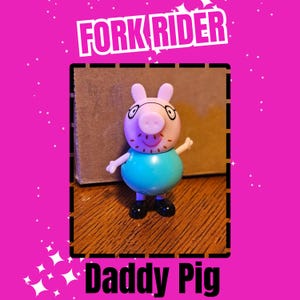 May include: A Daddy Pig figurine with a light pink face, a blue torso, and black shoes. The figurine has a pink snout, small ears, and is wearing glasses. The text "FORK RIDER" and "Daddy Pig" are displayed in white on a pink background.
