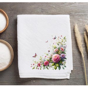 May include: White kitchen towel with a floral design featuring pink and purple flowers, green leaves, and butterflies. The design is in the corner of the towel.