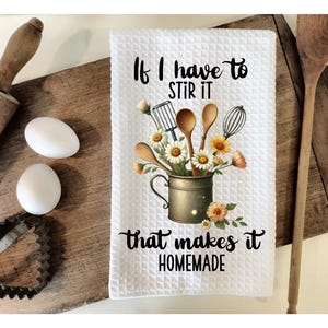 Può includere: Asciugamano da cucina bianco con un motivo floreale e il testo "Se devo mescolare, questo lo rende fatto in casa".