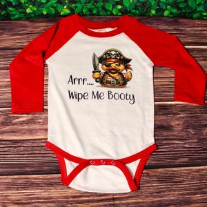 May include: White long-sleeve baby onesie with red sleeves. The onesie has a graphic of a pirate duck holding a sword and the text "Arr... Wipe Me Booty".