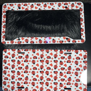 Może przedstawiać: Dwa białe ramki na tablice rejestracyjne z wzorem czerwonych biedronek i serc. Górna ramka jest pusta, a dolna ramka jest wypełniona wzorem.