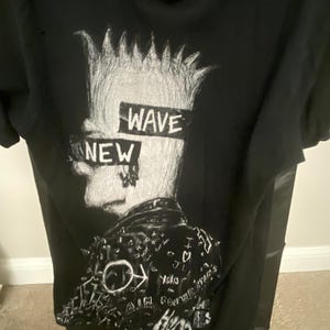 May include: Black t-shirt with a white graphic of a person with spiky hair. The graphic has the words "NEW WAVE" written across it. The person is wearing a leather jacket with various white markings.