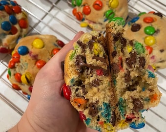 May include: A close-up of a freshly baked cookie cut in half, showing a soft interior with chocolate chips and colourful sweets. Several cookies are visible on a wire rack, each studded with vibrant sweets. The cookie's texture is soft and inviting.