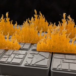May include: Five orange plastic flames on a grey textured surface. The flames are 3D printed and have a textured surface.