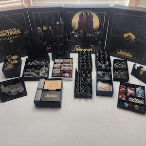 May include: A collection of black and gold storage boxes for the board game "Return to Dark Tower: Covenant". The boxes are filled with various game components, including miniatures, cards, and tokens.