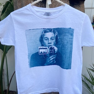 May include: White t-shirt with a blue and white image of a man holding a vintage camera. The image is a cyanotype print.