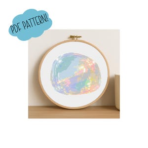 Puede incluir: Un patrón de punto de cruz de una esfera iridiscente colorida, colocada dentro de un aro de bordado de madera. El diseño presenta una mezcla de colores pastel. Un gráfico azul en forma de nube sobre el aro dice "PDF PATTERN!"