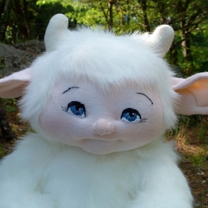 Könnte beinhalten: Ein weißes, flauschiges Wesen mit großen Ohren und blauen Augen. Das Wesen hat ein weiches, plüschiges Aussehen und ist aus Stoff gefertigt.