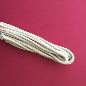 May include: A close-up of a white cotton rope, coiled and lying on a red surface.