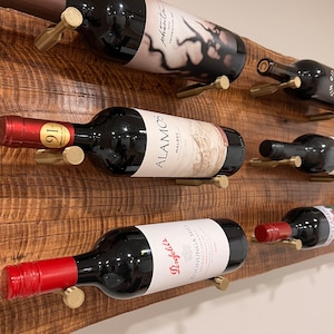 May include: A wooden wine rack with six bottles of wine. The rack is made of reclaimed wood and has a rustic look. The bottles are all different brands and colors. The rack is mounted on a wall.