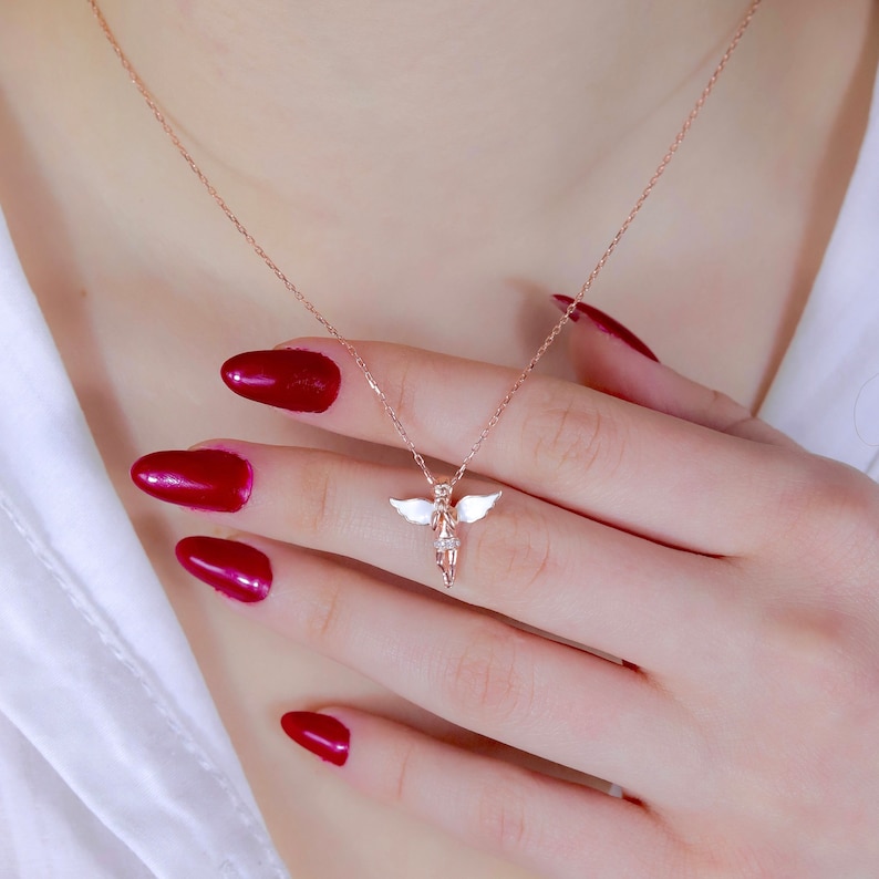 Puede incluir: Un collar de oro rosa con un delicado colgante de &aacute;ngel. El &aacute;ngel est&aacute; hecho de metal blanco y tiene un peque&ntilde;o diamante en el centro de su pecho.