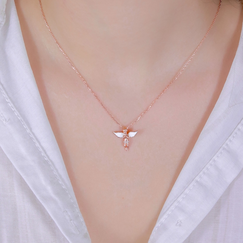 Puede incluir: Un delicado collar de oro rosa con un peque&ntilde;o colgante de &aacute;ngel de esmalte blanco. El &aacute;ngel tiene alas y est&aacute; de pie con los brazos extendidos.