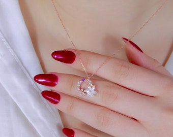 May include: Rose gold necklace featuring a delicate floral pendant. The pendant is a circular design with white flowers, clear and purple gemstones. The necklace is displayed on a white background.
