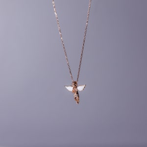 Puede incluir: Un collar de cadena de oro con un peque&ntilde;o colgante de &aacute;ngel. El &aacute;ngel tiene alas blancas y tiene las manos juntas en oraci&oacute;n.