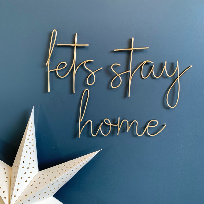 May include: Gold wire wall art with the words "Let's stay home" on a blue background. A white star with polka dots is in the lower left corner.