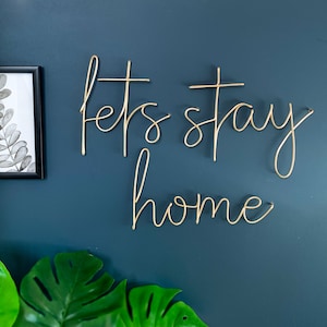 May include: Gold metal wall decor with the words "Let's stay home" in a cursive font.