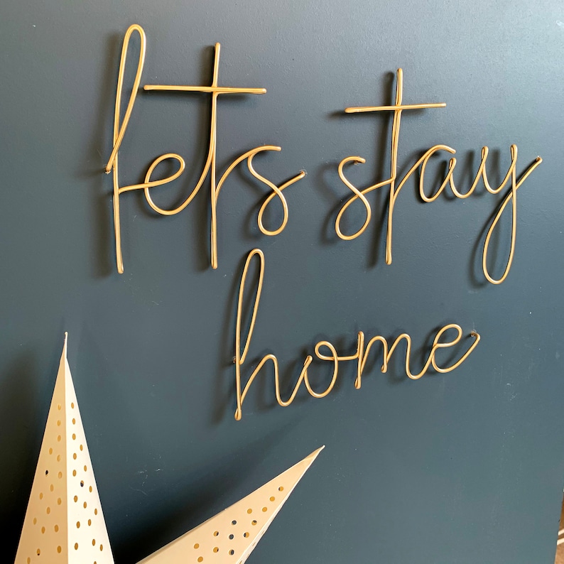 May include: Gold wire wall art with the words "Let's stay home" on a dark blue background.