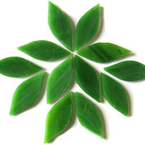May include: A collection of green, leaf-shaped glass tiles arranged in a circular pattern. The tiles are a vibrant green color and have a smooth, glossy finish. The arrangement resembles a stylized flower or sunburst design.