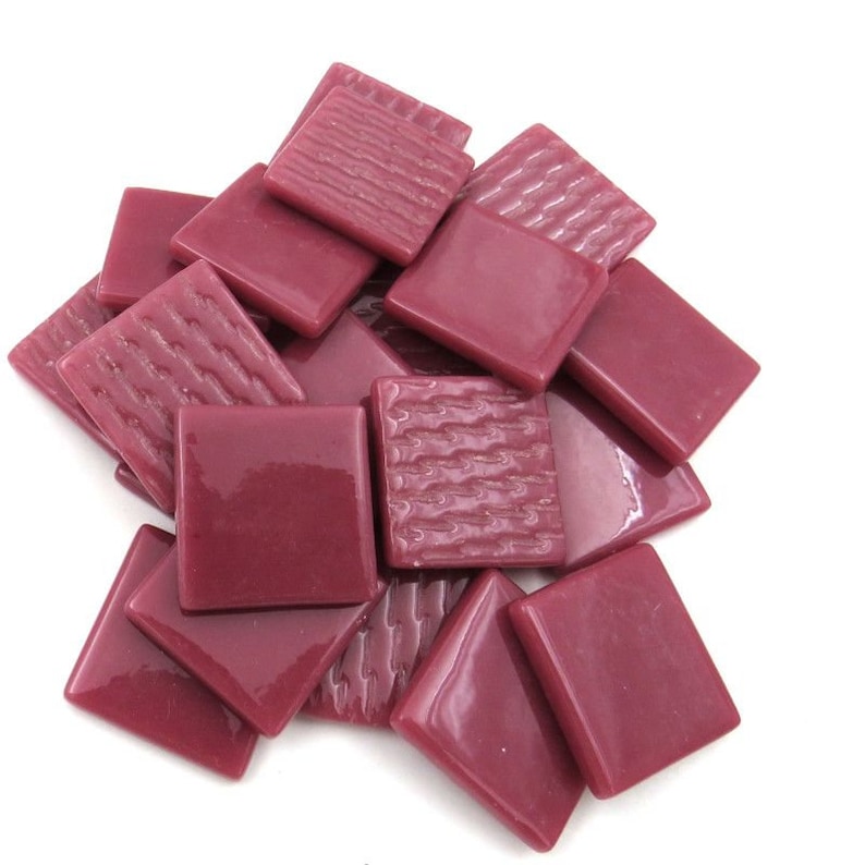 May include: A pile of small, square, burgundy glass tiles with a textured surface. The tiles are approximately 1 inch by 1 inch.