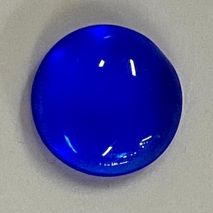 May include: A vibrant, round, cobalt blue gemstone with a smooth, polished surface. The gem reflects light, creating bright highlights. The object is set against a neutral background, emphasizing its color and form.