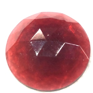 May include: A deep red, faceted, round glass gem. The gem has a shiny, reflective surface.