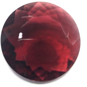 May include: A deep red gemstone with a faceted cut. The gemstone has a starburst pattern and a shiny, polished finish.