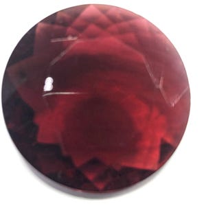 May include: A deep red gemstone with a faceted cut. The gemstone has a starburst pattern and a shiny, polished finish.
