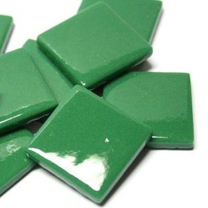 May include: A collection of small, square, glossy green tiles arranged in a loose, overlapping pile. Each tile features a smooth, reflective surface with uniform color and straight edges, creating a consistent appearance across the group.