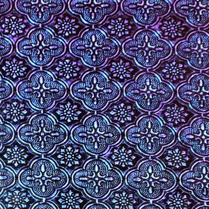 May include: A close-up of a textured, iridescent purple and blue patterned fabric with a repeating geometric design.