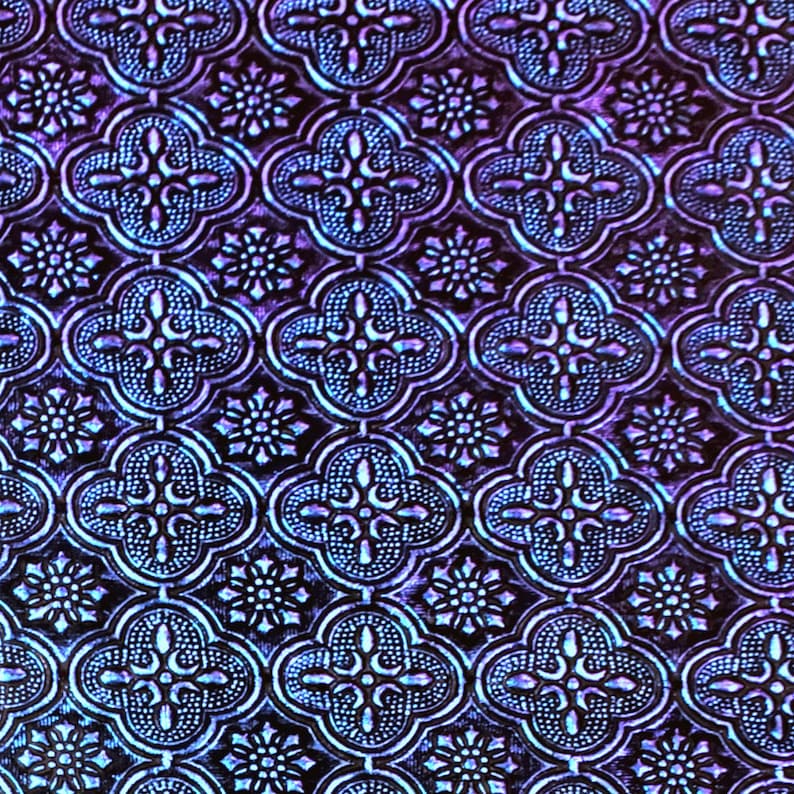 May include: A close-up of a textured, iridescent purple and blue patterned fabric with a repeating geometric design.