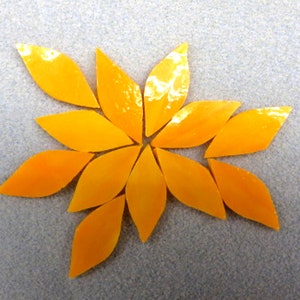 May include: A cluster of ten yellow glass mosaic tiles in the shape of leaves arranged in a starburst pattern.