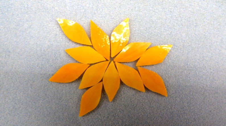 May include: A cluster of ten yellow glass mosaic tiles in the shape of leaves arranged in a starburst pattern.