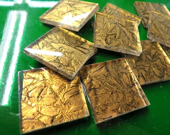 May include: A collection of small, square, gold-colored glass tiles with a textured, embossed pattern. The tiles have a metallic sheen and are arranged in a random pattern.