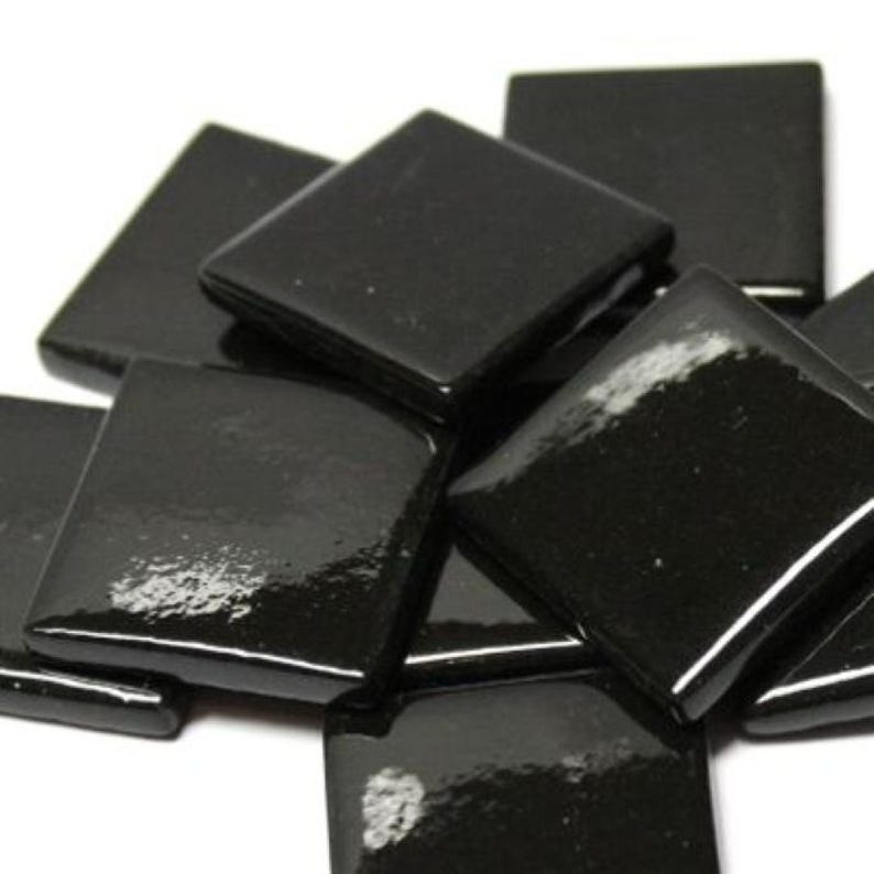 May include: A pile of black square glass tiles. The tiles are glossy and have a smooth surface.