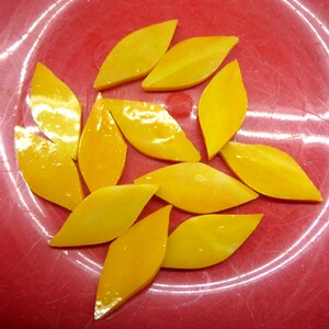 May include: A group of ten yellow glass leaf-shaped tiles on a red background.