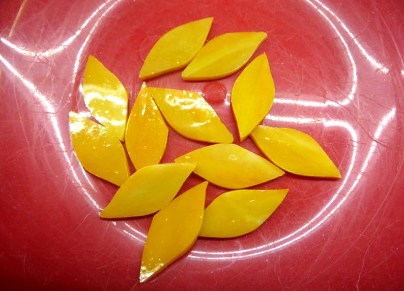 May include: A group of ten yellow glass leaf-shaped tiles on a red background.