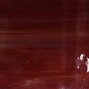 May include: A close-up of a deep red glass surface with subtle white streaks and a few white spots.