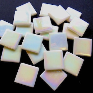 May include: A collection of small, square-shaped tiles with a smooth, glossy finish. Each tile features an iridescent, pearlescent white surface that reflects subtle rainbow hues, creating a shimmering effect across the group of individual pieces.