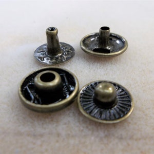May include: Four antique gold-toned metal snap fasteners with decorative details. The fasteners have a round base and a raised center.