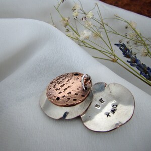 Op de afbeelding: Een zilveren bedel met een koperen schijf erop. De bedel is gegraveerd met de woorden "Be Kind".