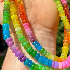 May include: A multi-strand necklace featuring small, round, translucent beads in a vibrant rainbow spectrum of colours including pink, orange, yellow, green, blue, and purple. The necklace is secured with a gold-toned metal lobster claw clasp.