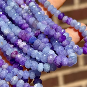 May include: A strand of faceted gemstone beads in shades of blue and purple. The beads are small and round, and they are strung together on a clear thread.