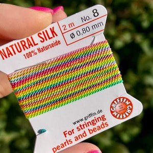 Könnte beinhalten: Eine Spule mit 2 Metern Naturseidenfaden, 0,80 mm Durchmesser, zum Fädeln von Perlen und Perlen. Die Spule ist mit "NATURAL SILK 100% Naturseide" und "No. 8" beschriftet.
