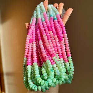 May include: Strands of colorful gemstone beads in shades of pink, green, and blue. The beads are small and round, creating a textured and vibrant appearance. The beads are held together, creating a cascading effect.