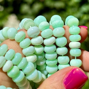 May include: A strand of light green opal beads. The beads are round and have a smooth, polished finish. They are strung on a clear thread.