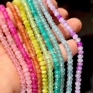 May include: Multiple strands of faceted, round gemstone beads arranged in a spectrum of colors including pink, orange, yellow, lime green, teal, light blue, and purple. Each strand features uniform, small, polished beads with a reflective surface.
